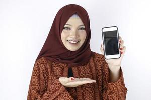 jonge Aziatische islam vrouw lacht wijzend op smartphone staande op een witte achtergrond. foto