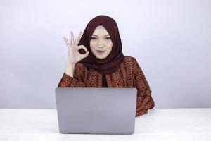 jonge aziatische islamvrouw lacht en is blij als ze op een laptop werkt met een ok handteken. foto