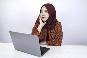 jonge aziatische islamvrouw kijkt serieus met een denkend gebaar op het gezicht op de voorkant van de laptop. foto