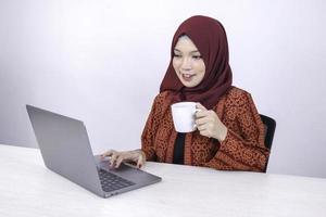mooie jonge aziatische islamvrouw werkt graag op een laptop terwijl ze in de witte kamer zit en koffie drinkt. foto