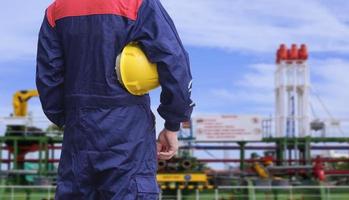 achteraanzicht en buik van ingenieur met gele veiligheidshelm met vage achtergrond van ruwe olietanker op scheepswerfgebied foto