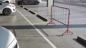 zonlicht en schaduw op oppervlak van stalen rode en witte verkeersbarrière met rij betonnen wielstops en witte markeringslijnen op cementvloer op parkeerplaats foto