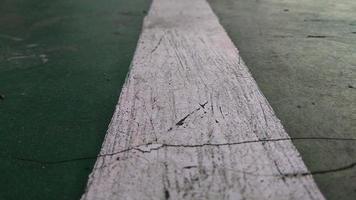close-up van een gekloofde witte lijn getekend op een groen-gebroken vloer op een openbaar sportveld. foto