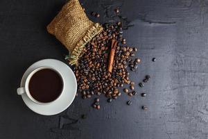 koffiebonen in bruine zak met koffiekopje op zwarte achtergrond. foto