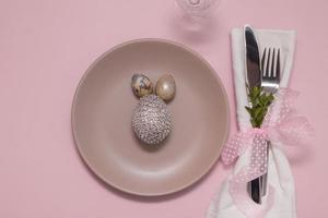 bord met eetgerei op een servet en een ei op een pastelroze achtergrond Pasen-menuconcept foto