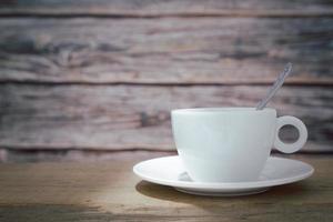 een witte koffiekop met een lepel in de kop en een schotel wordt op een houten plaat en op een houten ondergrond geplaatst. foto