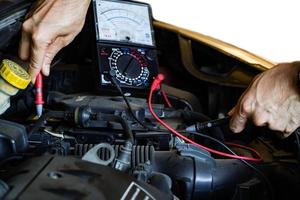 Aziatische mechanische autoreparatieprofessionals gebruiken een spanningsmultimeter om in autoreparatiediensten te werken. foto