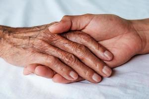 handen van de oude man en een mannenhand op het witte bed foto