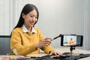 jonge aziatische vrouw vlogt zichzelf over schoonheidsproducten met het maken van een video voor haar blog over cosmetica met behulp van een telefooncamera thuis. foto