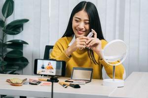 jonge aziatische vrouw vlogt zichzelf over schoonheidsproducten met het maken van een video voor haar blog over cosmetica met behulp van een telefooncamera thuis. foto