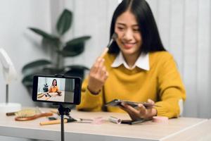 jonge aziatische vrouw vlogt zichzelf over schoonheidsproducten met het maken van een video voor haar blog over cosmetica met behulp van een telefooncamera thuis. foto