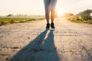 jonge sportieve fitness vrouw trail loopt op de landelijke weg in de zomer met zonsondergang achtergrond foto
