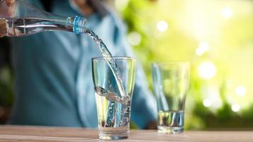 vrouw die drinkwater in het glas giet, verfrissend op groene tuinachtergrond. foto