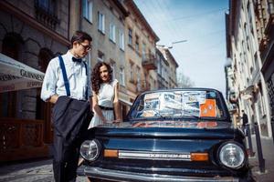 jong stel, vrouw en knappe man poseren in de buurt van zwarte retro auto foto
