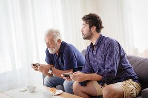 grootvader ouderling gelukkig geniet van een momentje plezier met zijn zoon thuis die samen een mobiel spel speelt. foto