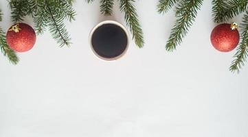 christmas coffee.top uitzicht, een kopje koffie en twee rode ballen met kerstboom takken op witte achtergrond, copyspace in de naar beneden. foto