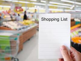 vrouwelijke hand met boodschappenlijstje papier op supermarkt wazige achtergrond foto