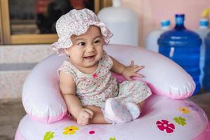portret van een klein Aziatisch babymeisje dat lacht en kijkt naar of iets of haar moeder op een springstoel tijdens de pandemie van het coronavirus covid-19, foto