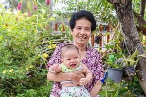 gelukkige grote lachende kindjongen en senior vrouw met schattige babyjongen in bloemrijke tuin. foto