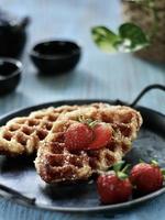 hoge hoekmening van croffle, moderne afhaal- of bezorgmaaltijden, geserveerd met aardbeien op het vintage bord en de blauwe tafel. foto