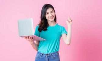 jonge aziatische vrouw die laptop op roze achtergrond gebruikt foto