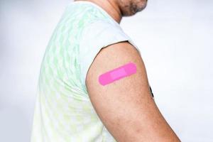 aan de arm van de man is een roze verband bevestigd. concept voor eerste hulp na coronavirus covid-19 vaccinatie, en professioneel, medisch, naald, bloed, kanker. close-up, witte onscherpe achtergrond foto