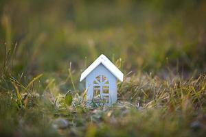 cijfers van kleine witte houten huizen op het gras close-up. het huisje ligt in een landelijke omgeving en dorp, bouwen, project, verhuizen, hypotheek, huren en onroerend goed kopen. kopieer ruimte foto