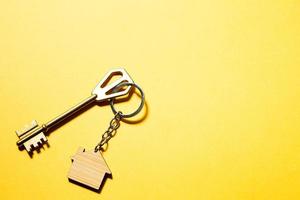 sleutelhanger in de vorm van een houten huis met sleutel op een gele achtergrond. bouwen, ontwerp, project, verhuizing naar nieuwe woning, hypotheek, huur en aankoop onroerend goed. kopieer ruimte foto