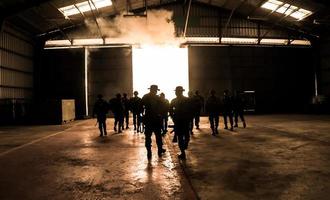 silhouetten van legersoldaten in de mist tegen een zonsondergang, mariniersteam in actie, omringd door vuur en rook, schietend met aanvalsgeweer en machinegeweer, aanvallende vijand foto