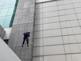 foto van een werknemer die de buitenkant van het gebouw schoonmaakt, hangend aan een veiligheidstouw