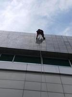 foto van een werknemer die de buitenkant van het gebouw schoonmaakt, hangend aan een veiligheidstouw