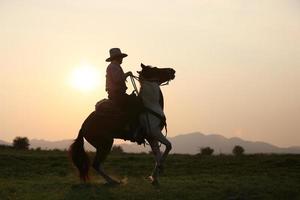 silhouetcowboy te paard tegen een prachtige zonsondergang, cowboy en paard bij het eerste licht, berg, rivier en levensstijl met natuurlijke lichte achtergrond foto