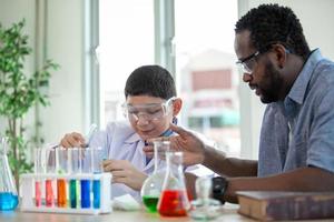 kleine jongen mengt chemicaliën in bekers. enthousiaste leraar legt scheikunde uit aan kinderen, scheikundestudent toont nieuw experiment aan leraar natuurkunde foto