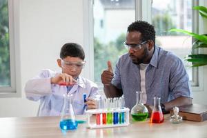 kleine jongen mengt chemicaliën in bekers. enthousiaste leraar legt scheikunde uit aan kinderen, scheikundestudent toont nieuw experiment aan leraar natuurkunde foto