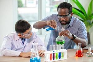 kleine jongen mengt chemicaliën in bekers. enthousiaste leraar legt scheikunde uit aan kinderen, scheikundestudent toont nieuw experiment aan leraar natuurkunde foto