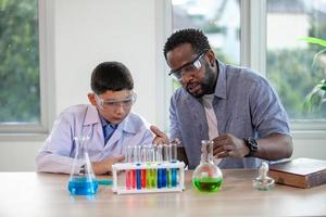 kleine jongen mengt chemicaliën in bekers. enthousiaste leraar legt scheikunde uit aan kinderen, scheikundestudent toont nieuw experiment aan leraar natuurkunde foto