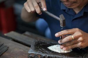 zilversmid met hamers en staal gegraveerd patroon op zilveren plaat voor handgemaakte accessoire foto