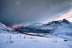 besneeuwde bergketen met verlichte stad aan de kust in blizzard