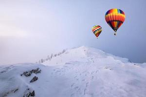 kleurrijke heteluchtballonnen vliegen op sneeuwheuvel met blizzard foto