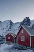 rood houten huisje aan de kust met besneeuwde berg en de maan in reine village op de lofoten-eilanden foto