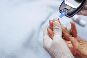 arts draag handschoenen met lancet op vinger voor het controleren van de bloedsuikerspiegel met een glucosemeter. foto