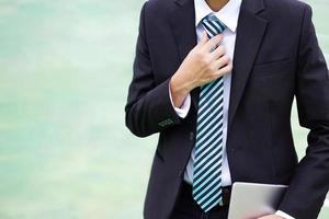 zakenman in een pak dat een tablet vasthoudt en een stropdas aanpast. foto