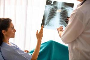 vrouwelijke arts toont afbeelding van röntgenfilm aan vrouwelijke patiënt en legt haar uit. foto