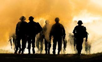 silhouetten van legersoldaten in de mist tegen een zonsondergang, mariniersteam in actie, omringd door vuur en rook, schietend met aanvalsgeweer en machinegeweer, aanvallende vijand foto