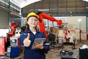 professionele jonge industriële fabrieksvrouw werknemer die met machineonderdeel werkt, industriële apparatuur en robotarmen controleert en test in grote elektrische elektronicadraad en fabriek foto