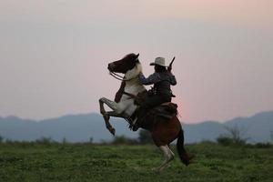 silhouetcowboy te paard tegen een prachtige zonsondergang, cowboy en paard bij het eerste licht, berg, rivier en levensstijl met natuurlijke lichte achtergrond foto