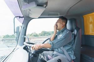 professionele vrachtwagenchauffeur, volwassen man, veiligheidsgordel geeuwen en slaperig. jonge man werknemer heeft lange tijd vertrouwen in de veiligheid van het transport- en bezorgbedrijf. foto