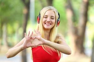 mooie blonde vrouw staande tijdens het luisteren naar muziek op de koptelefoon in het park. foto