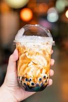 jong meisje houdt en toont een kopje bruine suiker gearomatiseerde tapioca parel bubbel melkthee op de avondmarkt van de achtergrond van taiwan, close-up, bokeh foto