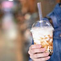 jong meisje in spijkerjasje drinkt bruine suiker gearomatiseerde tapioca parel bubbel melkthee met glas stro in avondmarkt van taiwan, close-up, bokeh foto